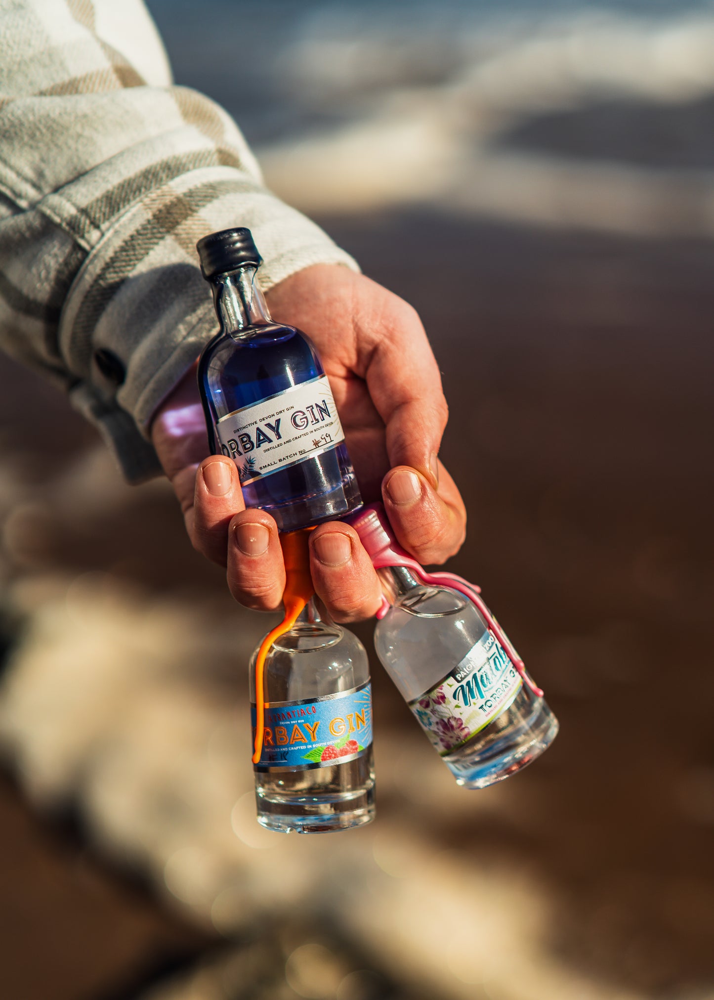 three mini bottles of gin in a hand at the beach