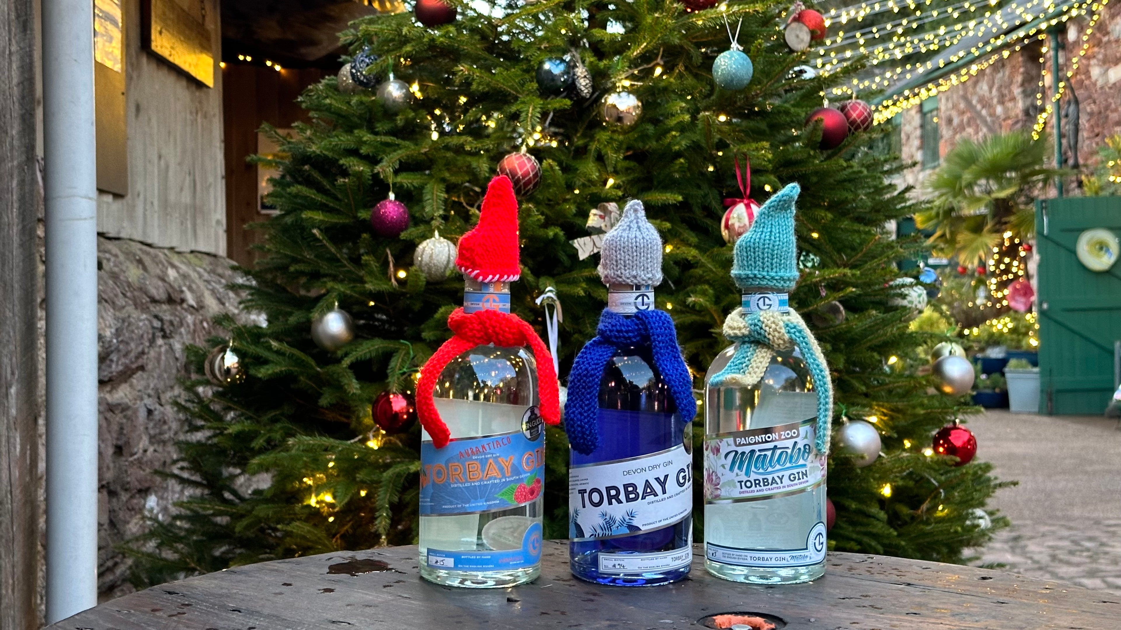 Three bottles of torbay gin in front of bauble filled Christmas tree in Cockington